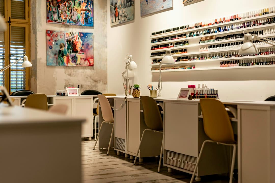Bancada de manicure com cadeiras amarelas e parede de esmaltes organizados por cor