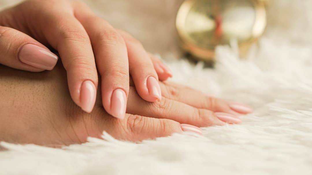 Mãos com unhas em tom rosado claro sobre manta felpuda creme